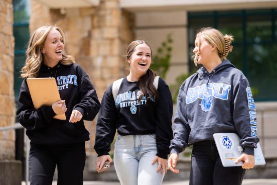 Three students wearing SSU sweatshirts and looking at each other laughing