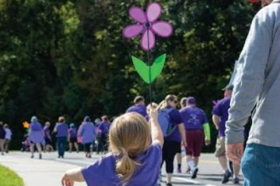 Child wearing purple shirt and holding a purple flower in the air