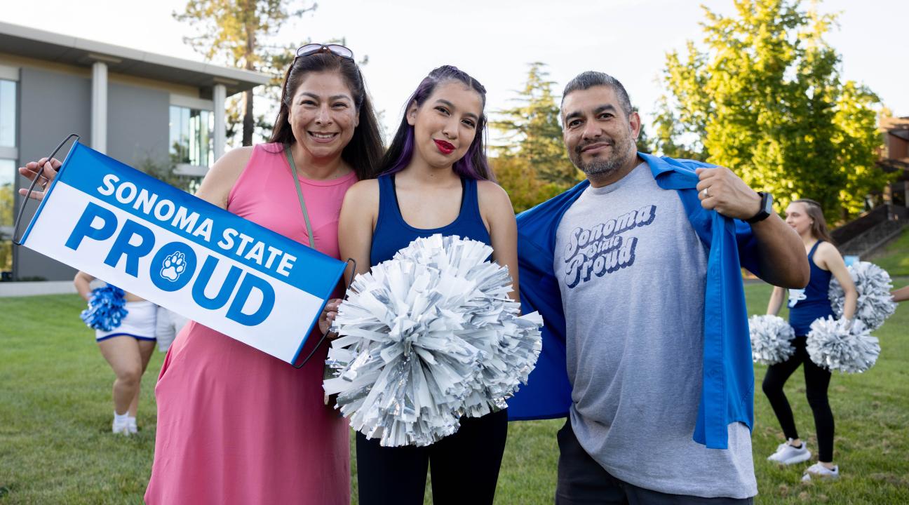 Two parents and a student smiling and holding a Sonoma State Proud Banner