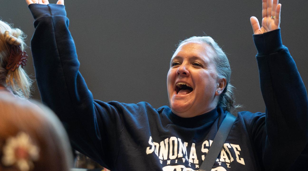 Person with hands up in the air cheering and wearing an alumni sweatshirt