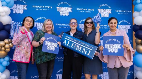 Group of fauclty and staff holding thank you signs and alumni signs