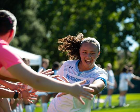 Women's soccer playing high fiving players with excitement on her face