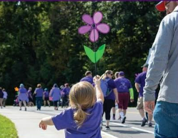 Child wearing purple shirt and holding a purple flower in the air