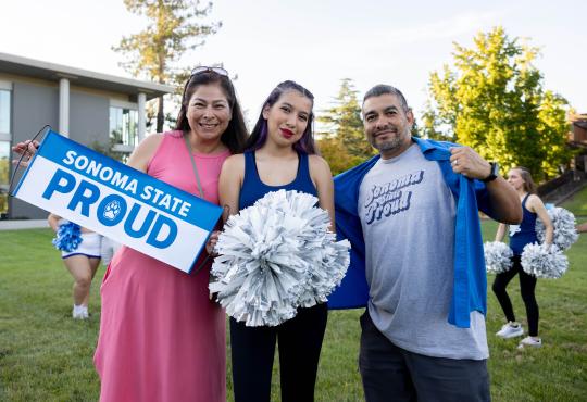Two parents and a student smiling and holding a Sonoma State Proud Banner