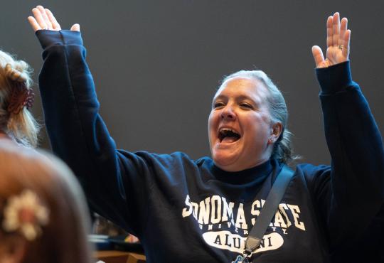Person with hands up in the air cheering and wearing an alumni sweatshirt