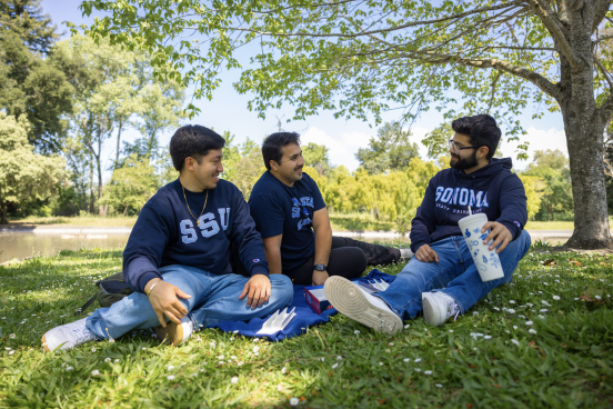 Three students sitting at lakes on a blanket